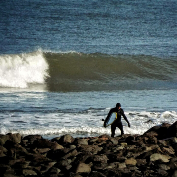 surfer with small wave breaking down lynmouth point in the bcakground